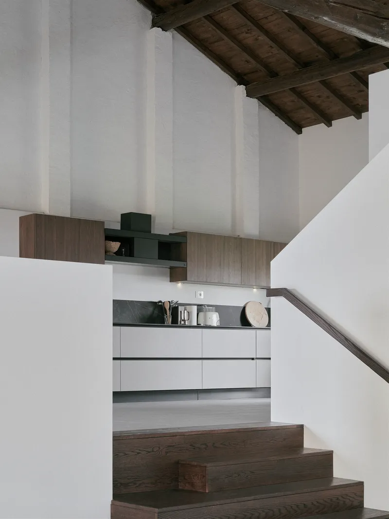 Kitchen glimpsed beyond timber staircase treads under the sloped wooden ceiling
