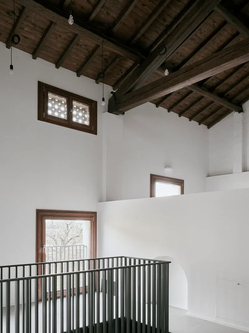 Double-height space with metal railing balcony and timber-framed windows overlooking bare winter trees