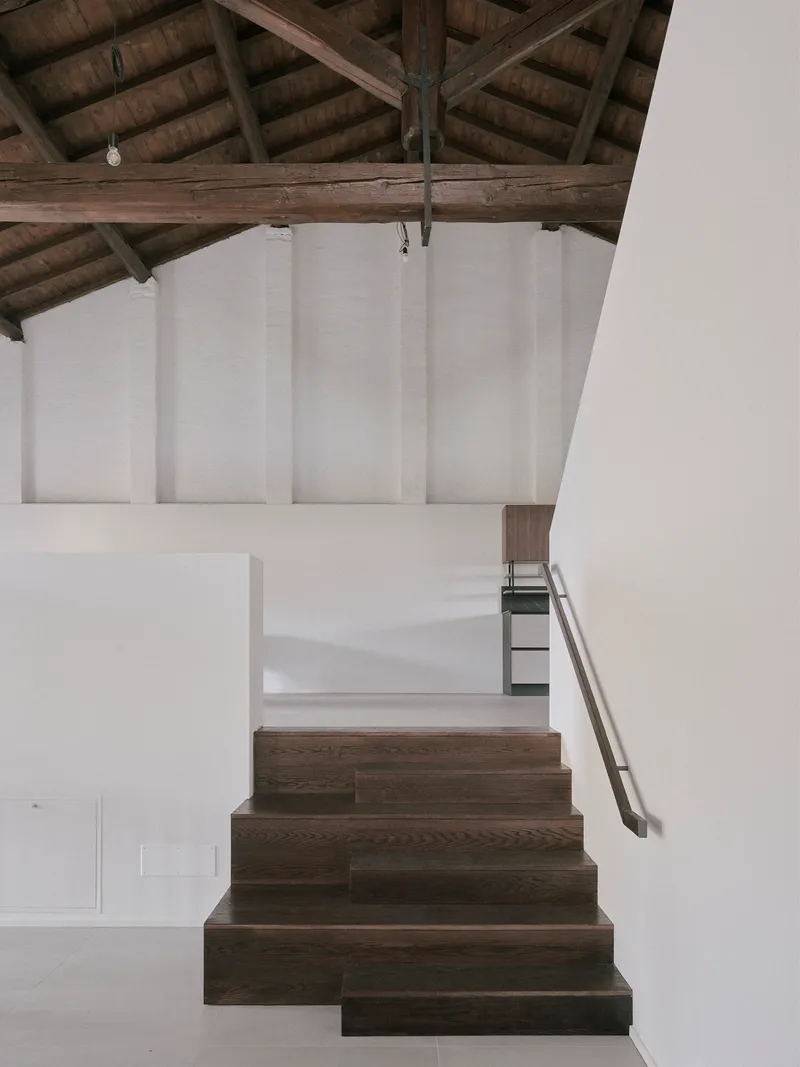 Dark oak staircase ascending toward white plaster walls beneath heavy timber roof trusses