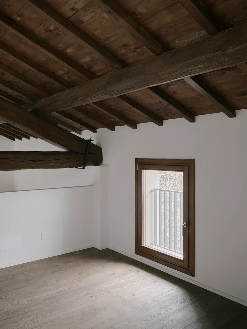 Timber-framed casement window in white plaster wall under exposed beam ceiling with concrete floor