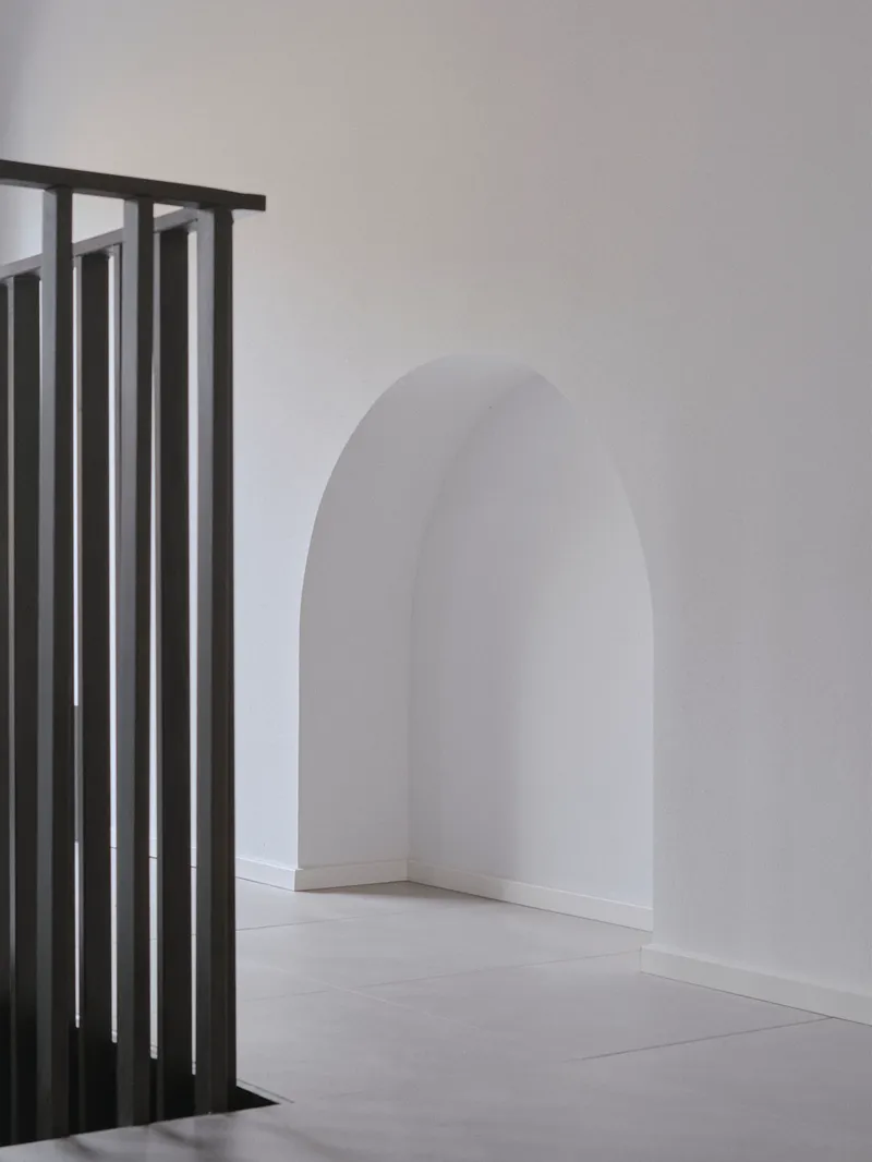 Metal slat balustrade beside an arched doorway with white plaster walls and pale flooring