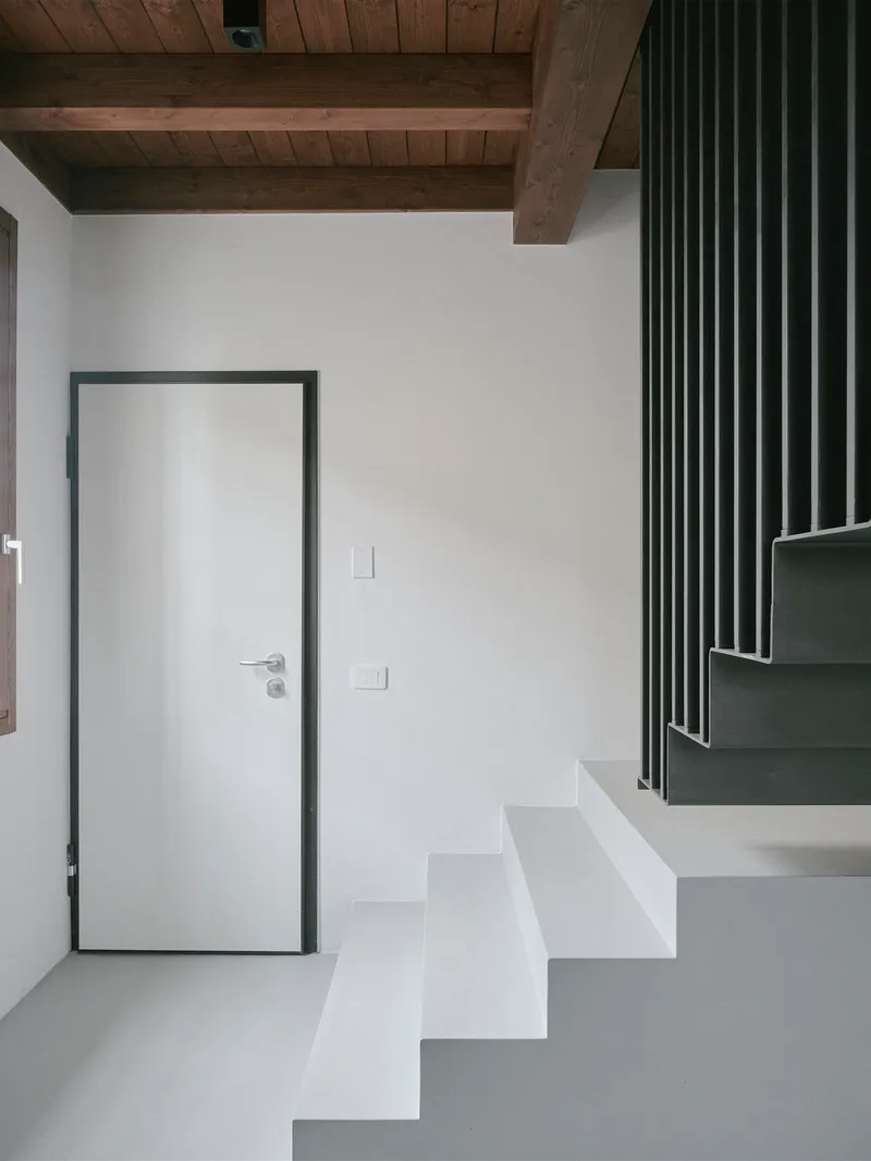 Entryway with white door beneath exposed timber beams and a staircase with metal balustrade