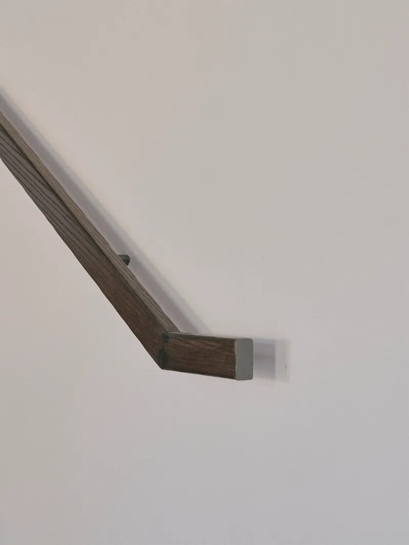 Close-up of a timber handrail with metal bracket mounting against a white wall