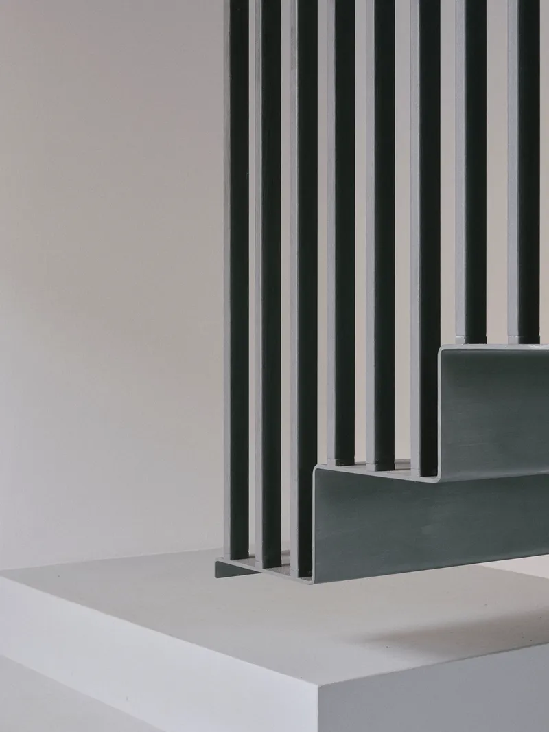 Detail of grey stairs with vertical metal rods passing through the treads and landing