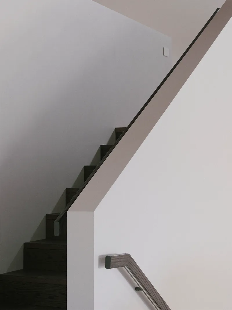 Interior view of cantilevered staircase with thin metal handrail ascending along white walls