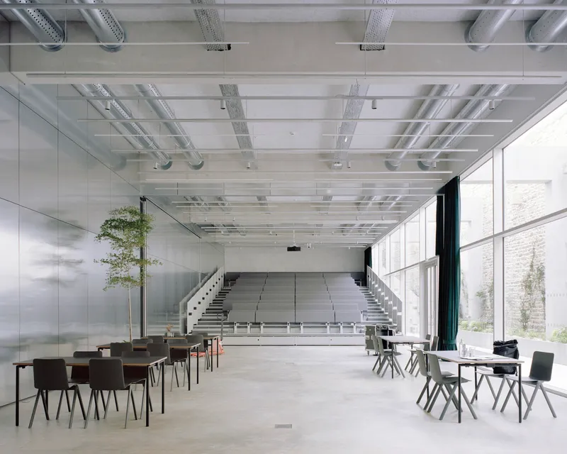 Retractable tiered seating emerging from the floor beneath a gridded ceiling with exposed mechanical systems