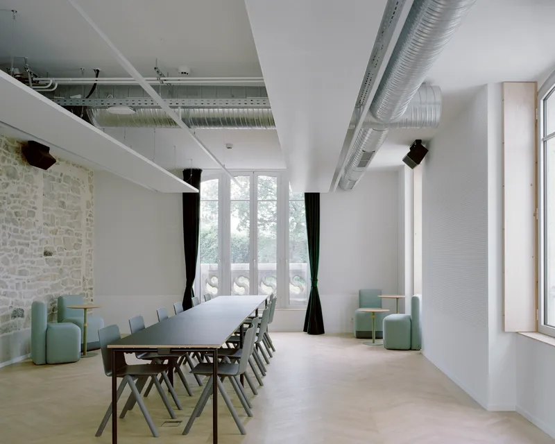 Meeting room with exposed stone wall, suspended ductwork, long white table, and green upholstered seating
