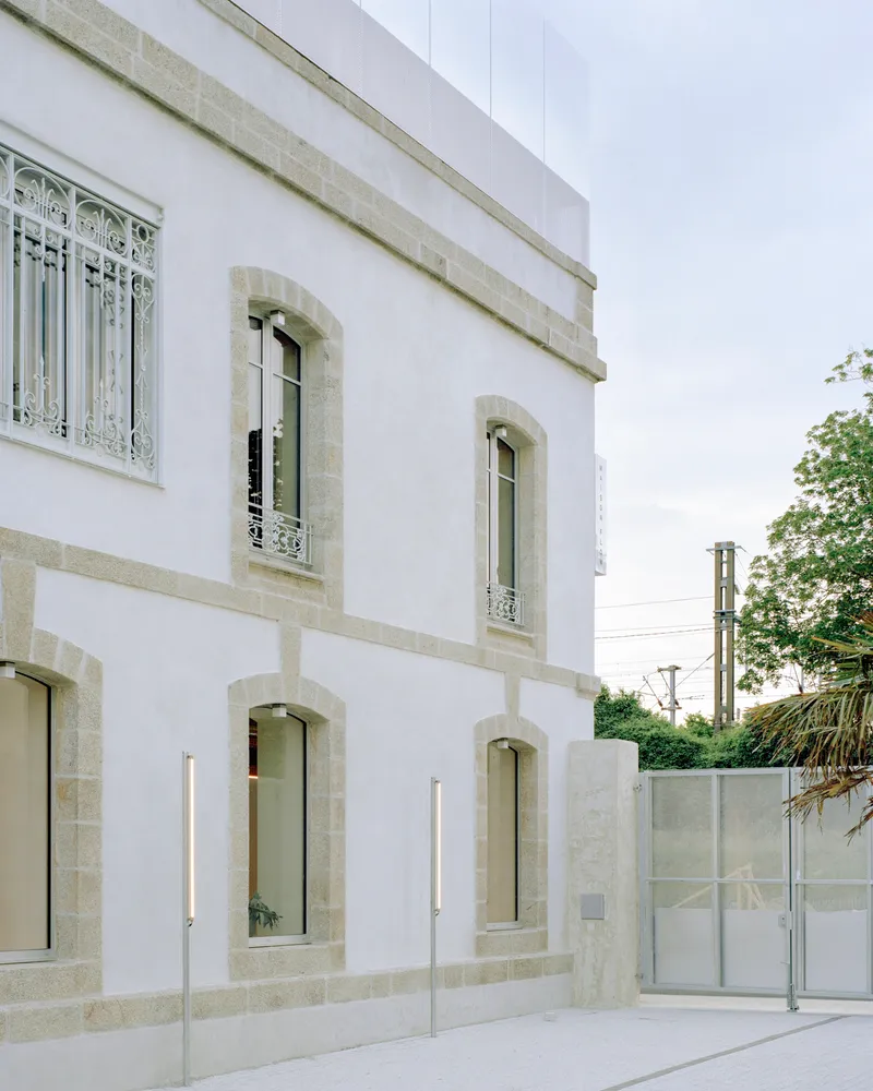 White stucco facade with stone-framed arched windows and decorative wrought iron grilles under an overcast sky