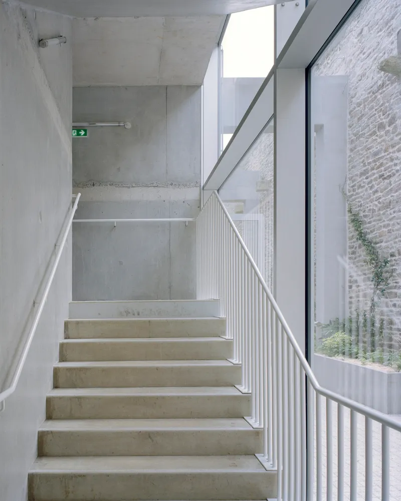 Concrete staircase with white metal balustrade and skylight above in diffused daylight