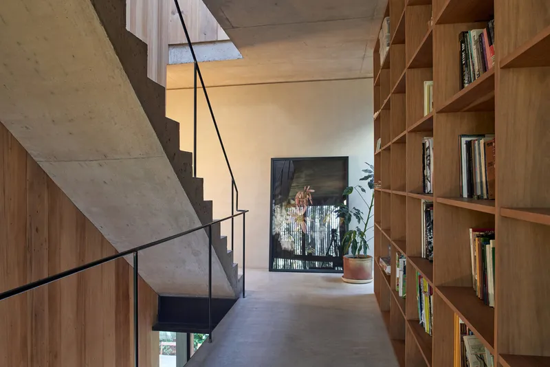Concrete stair with black steel railing ascending past floor-to-ceiling timber bookshelves