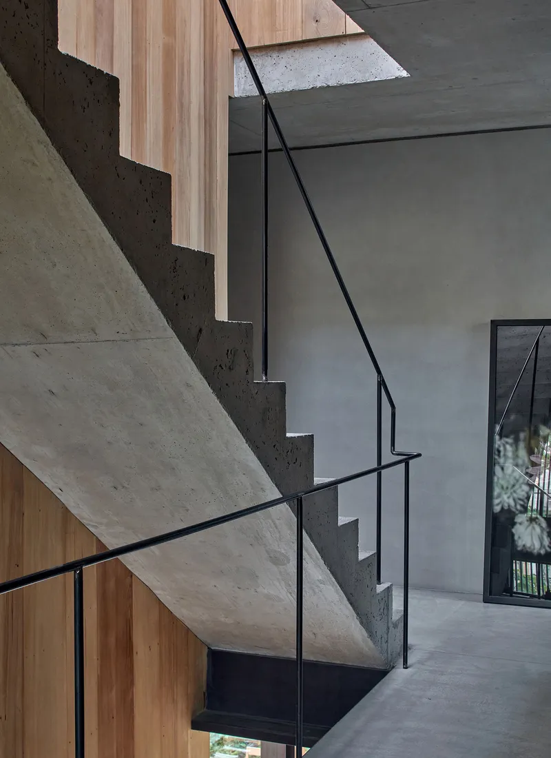 Close-up of cantilevered concrete stair treads with minimal black steel handrail against timber cladding