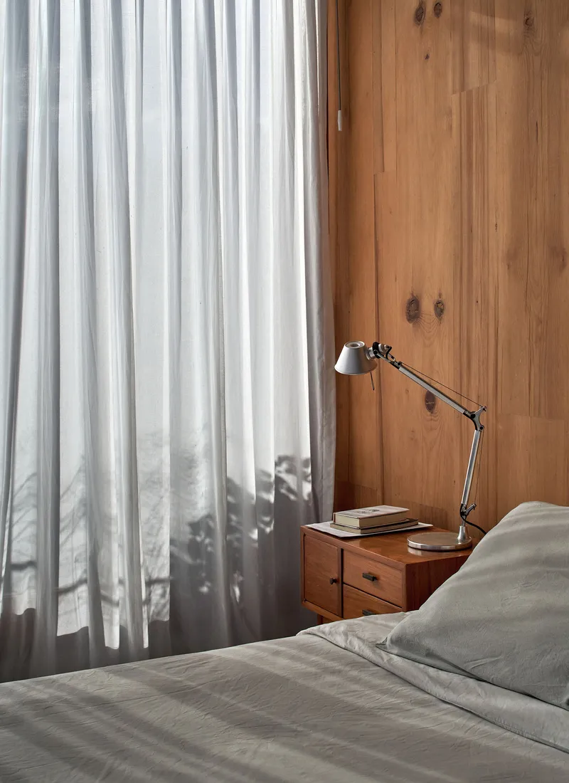 Bedside detail showing a wooden nightstand with articulated lamp against corrugated metal and timber walls