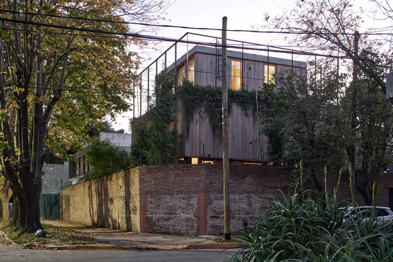 Street view of the timber-clad upper volume atop a brick retaining wall at twilight