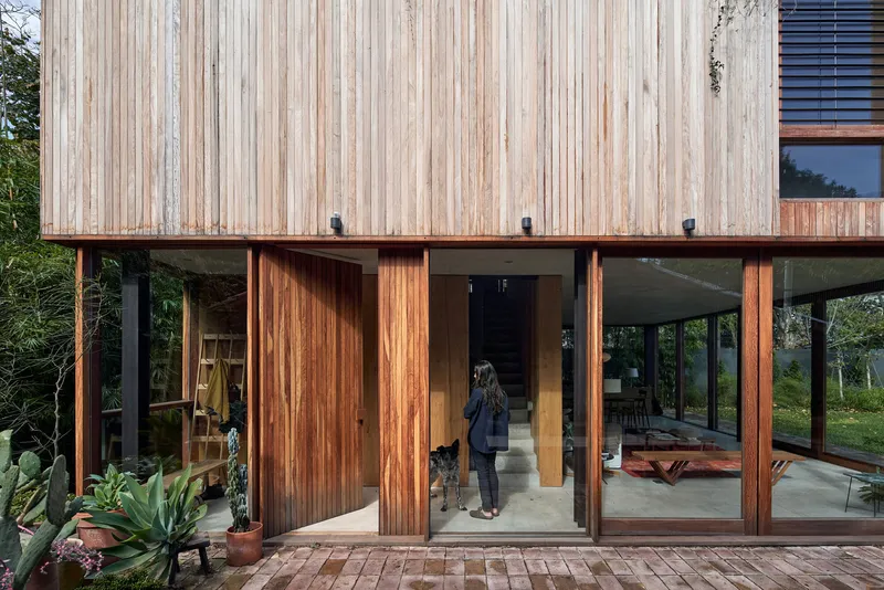 Ground level entrance with sliding timber doors, steel columns and a figure with dog entering at dusk