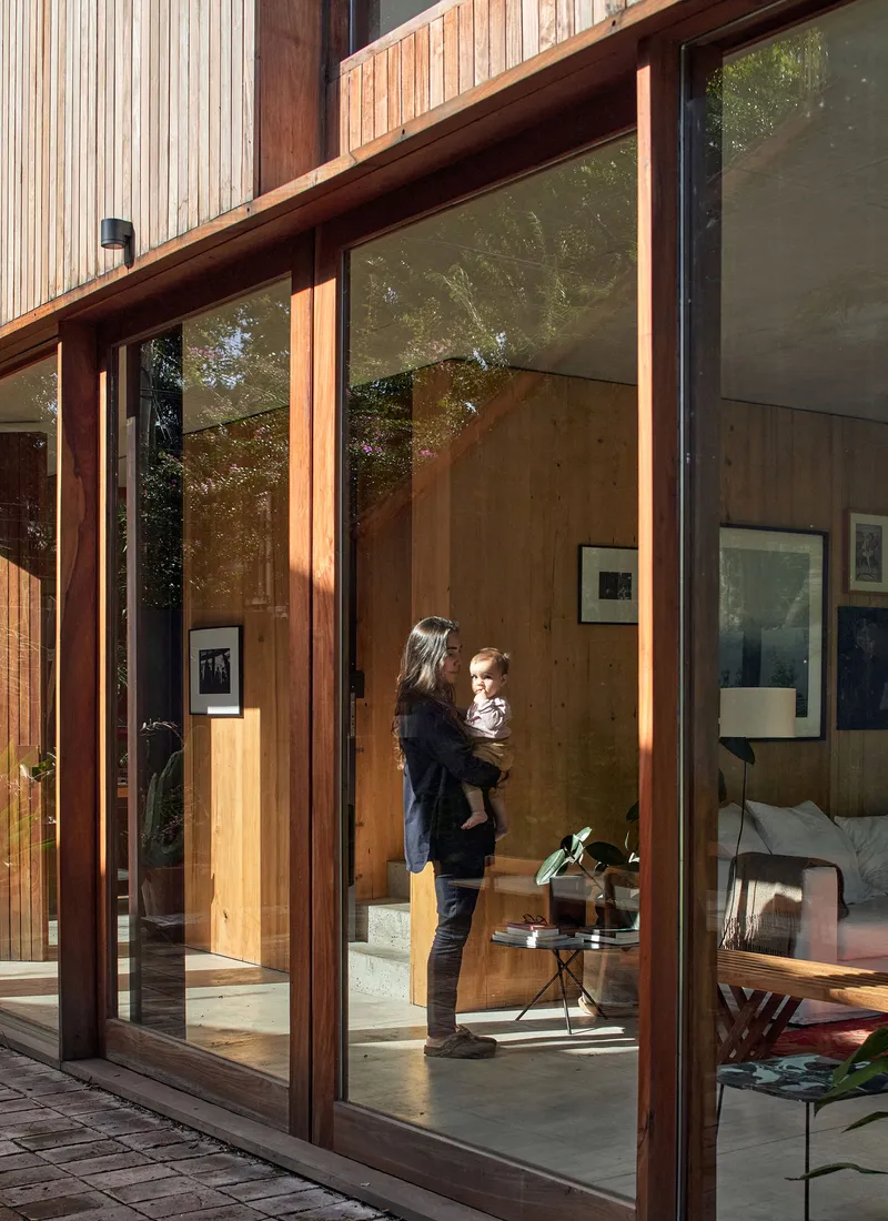 Timber-framed glass doors with parent holding child on polished concrete floor in afternoon sunlight