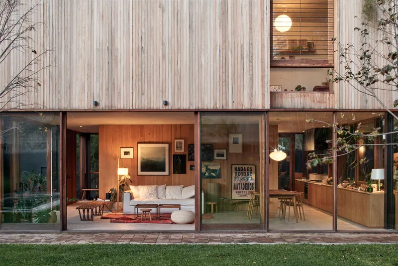 Floor-to-ceiling glazed walls opening living spaces to brick patio and lawn at dusk