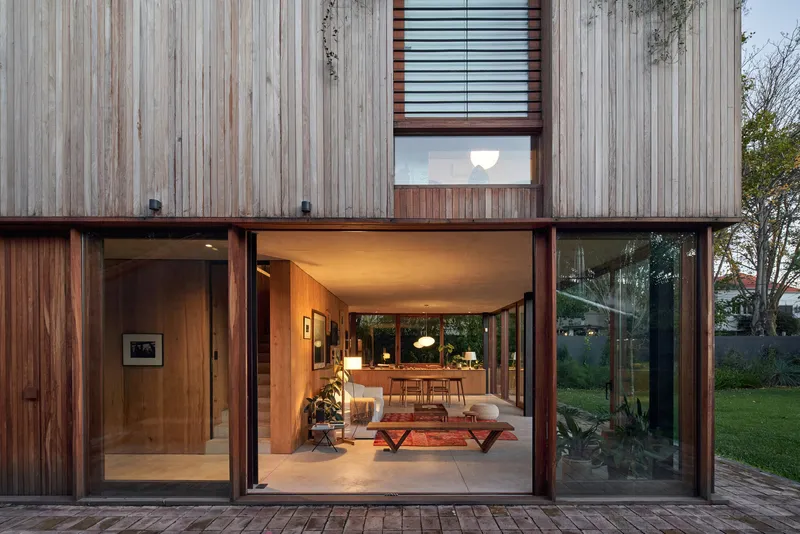 Open timber-framed threshold looking through living room to garden at twilight