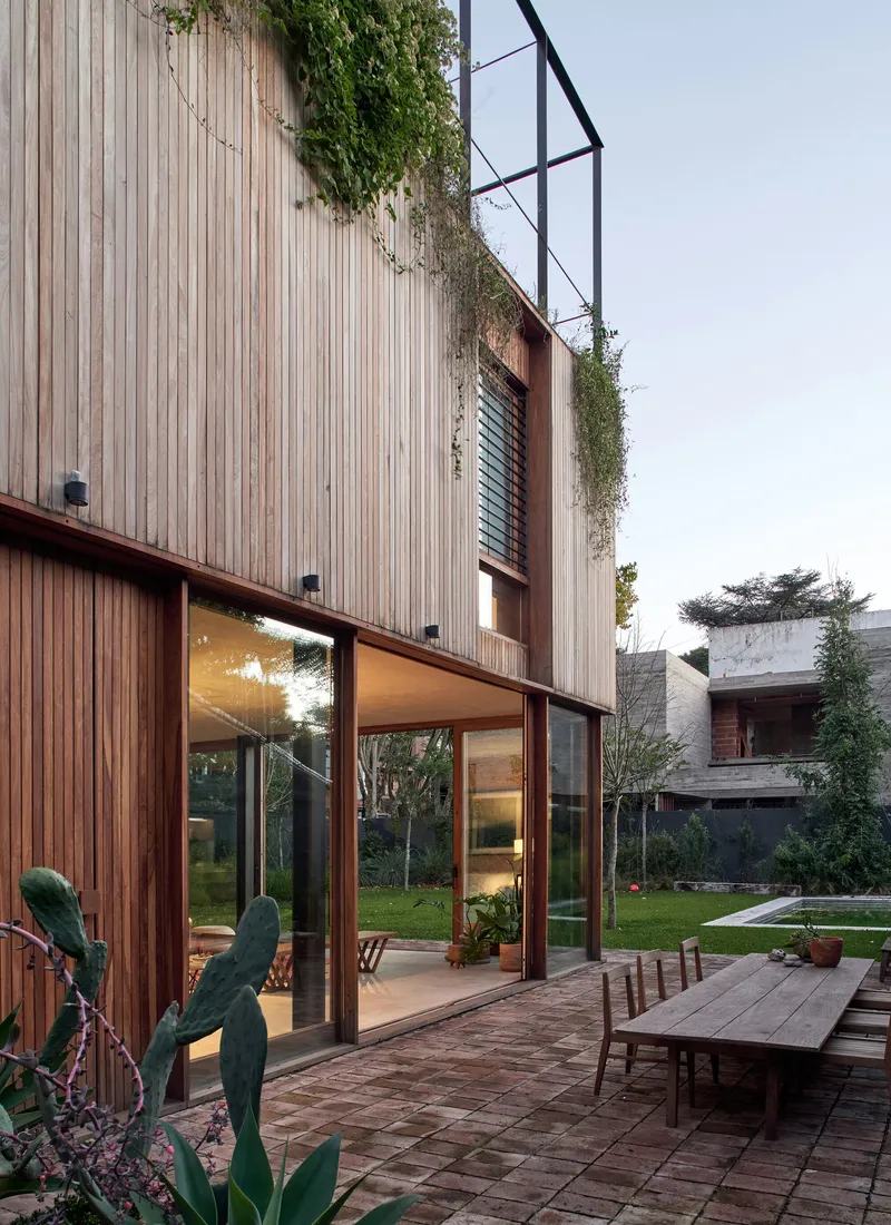 Vertical wood-slat facade with green roof plantings above full-height glazing and a terrace at dusk