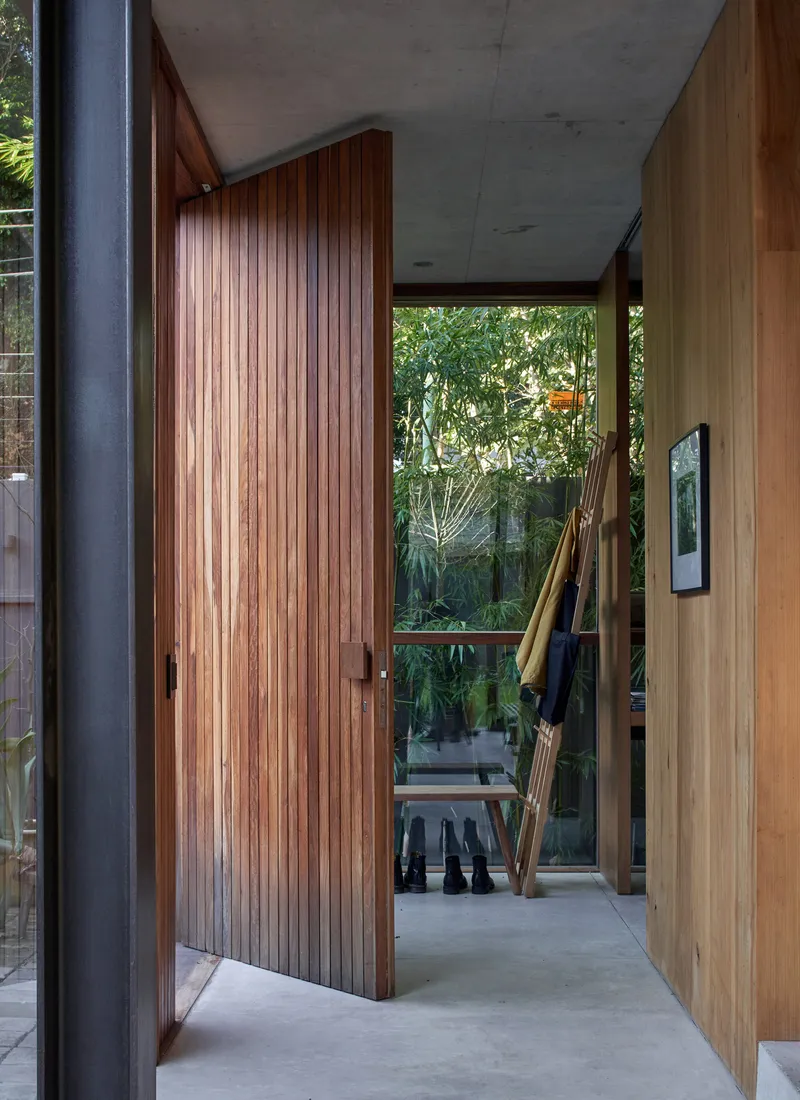 Covered entry corridor with concrete ceiling, timber slat door and garden view beyond