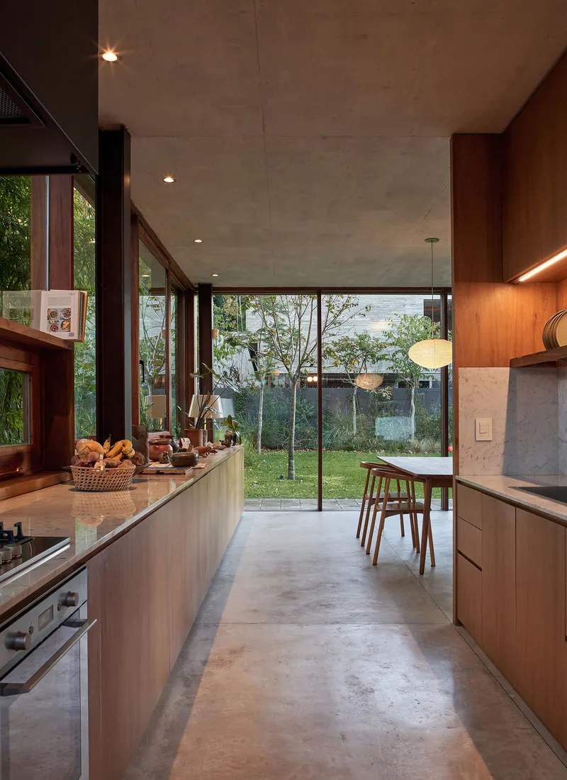 Kitchen with timber cabinetry and concrete floor opening to garden courtyard through glazed wall