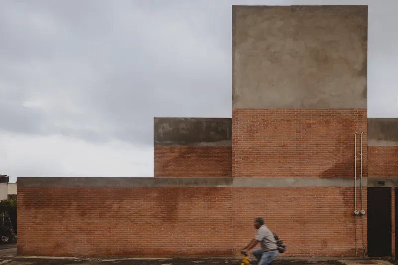 Street elevation of layered brick and concrete volumes with a cyclist passing by
