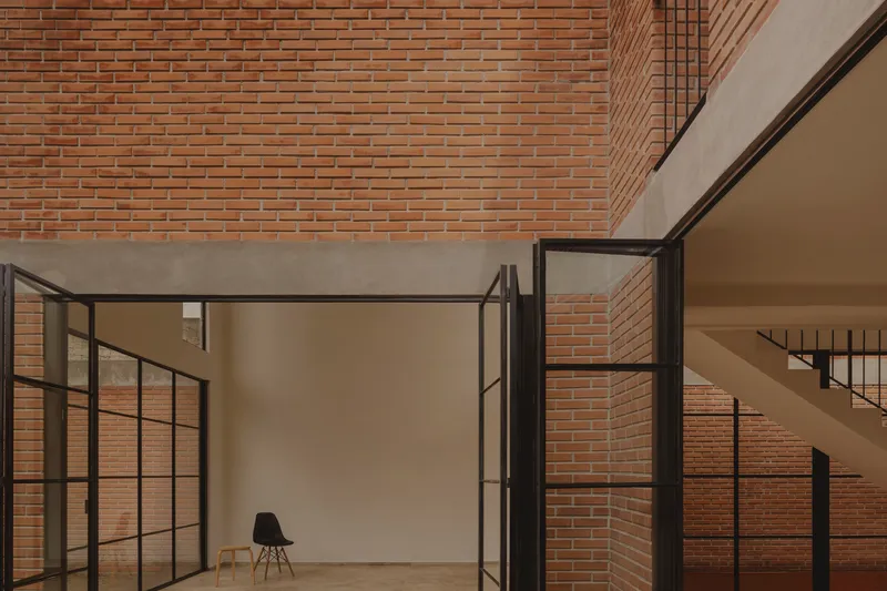 Steel-framed opening to a room with a single black chair against exposed brick walls