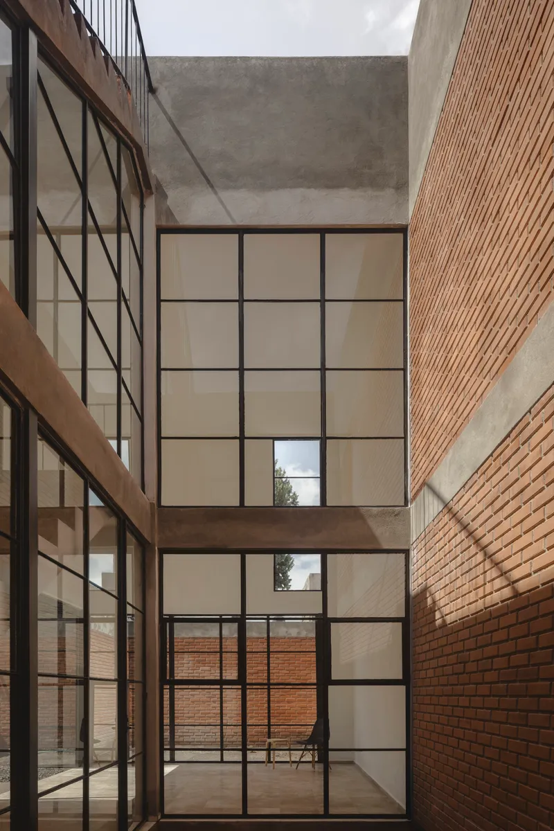 Vertical courtyard with stacked steel-framed windows between brick and concrete surfaces