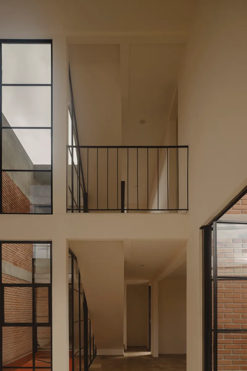 Double-height interior void with black steel framed windows and railings overlooking brick walls