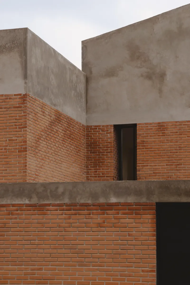 Staggered exterior volumes in red brick and poured concrete with a narrow vertical door opening