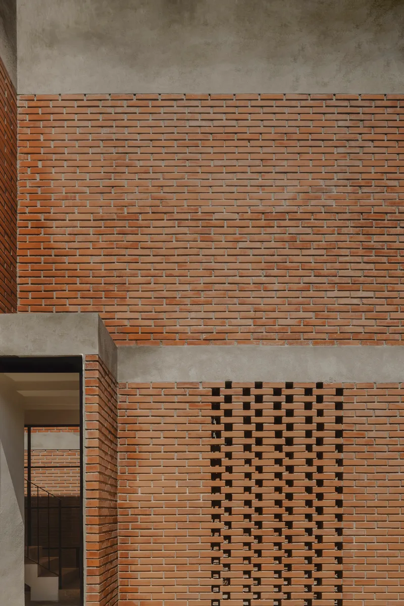Brick facade detail with patterned ventilation opening and concrete band wrapping the corner balcony