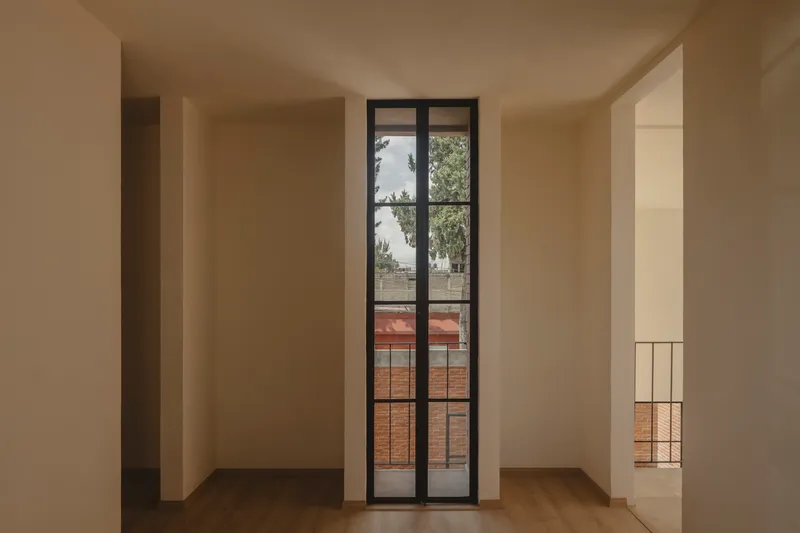 Interior room with tall steel framed door opening to balcony overlooking tree canopy and brick rooftops