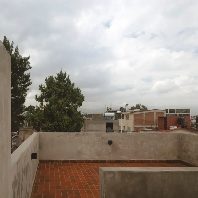 Rooftop terrace with red clay tile flooring and concrete parapet walls under overcast sky
