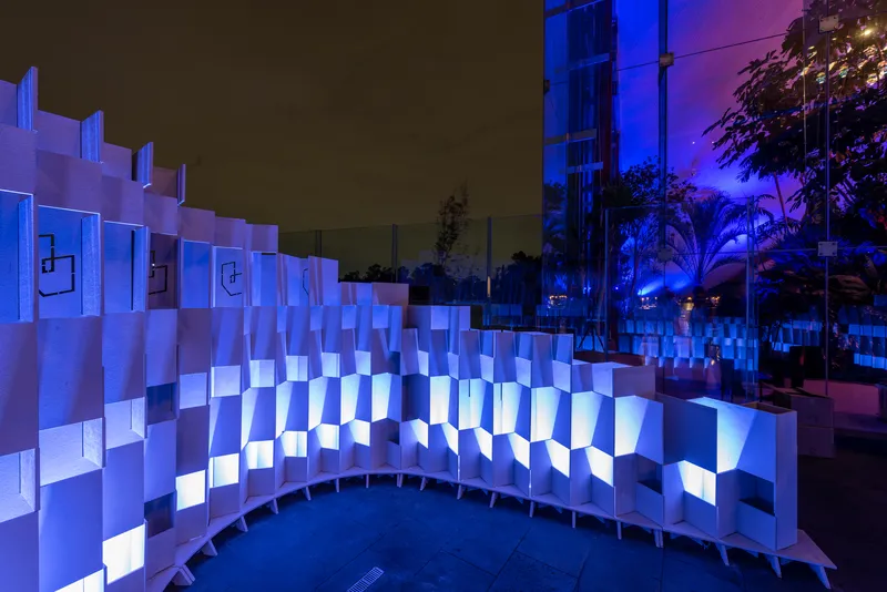 Curved wall of illuminated white panels with blue uplighting beside palm trees at night