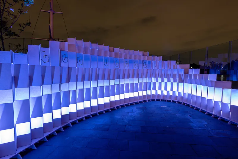Pixelated facade of backlit translucent panels forming a curved perimeter wall at dusk