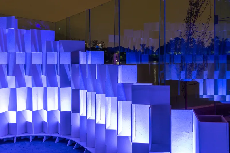 Detail of stepped translucent panel wall with blue lighting beneath a glazed canopy