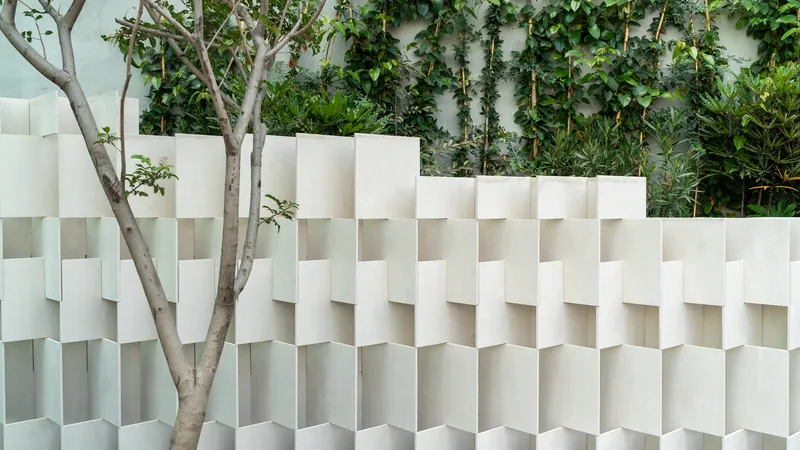 White textured wall system with projecting fins adjacent to climbing vines and a slender tree trunk