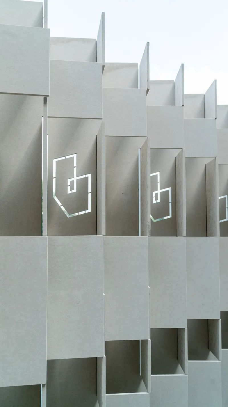Stepped facade featuring staggered concrete volumes with recessed geometric logo cutouts under overcast sky