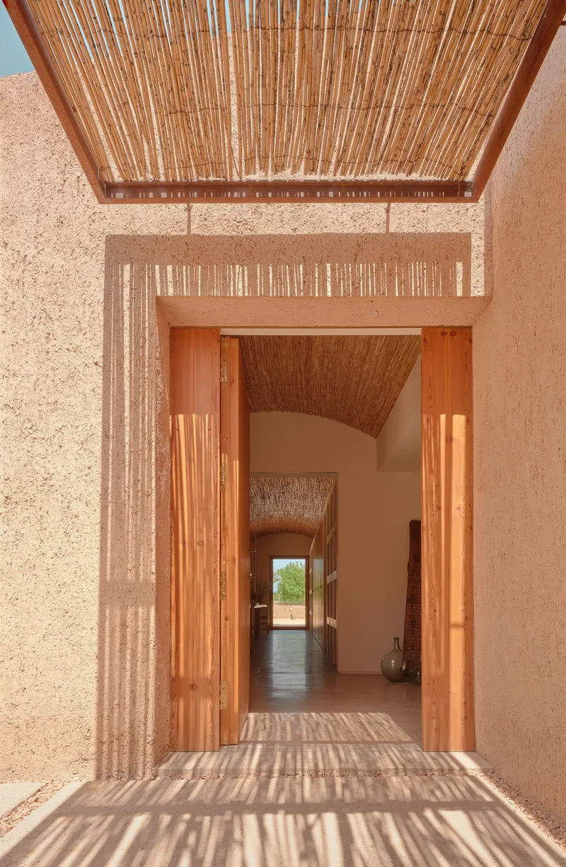 Entry doorway with timber frame and bamboo screen casting striped shadows across the threshold under midday sun