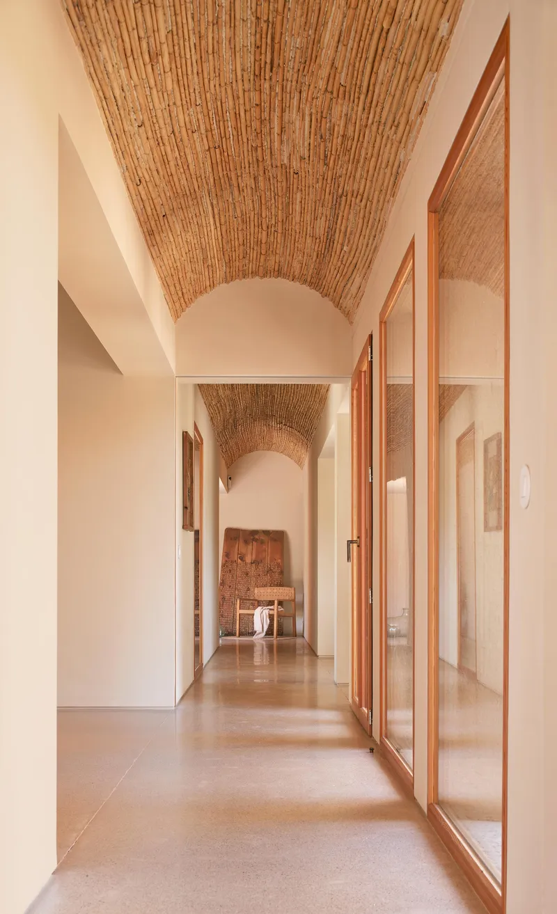 Corridor with vaulted bamboo ceiling, polished concrete floor, and timber-framed glass doors along one wall