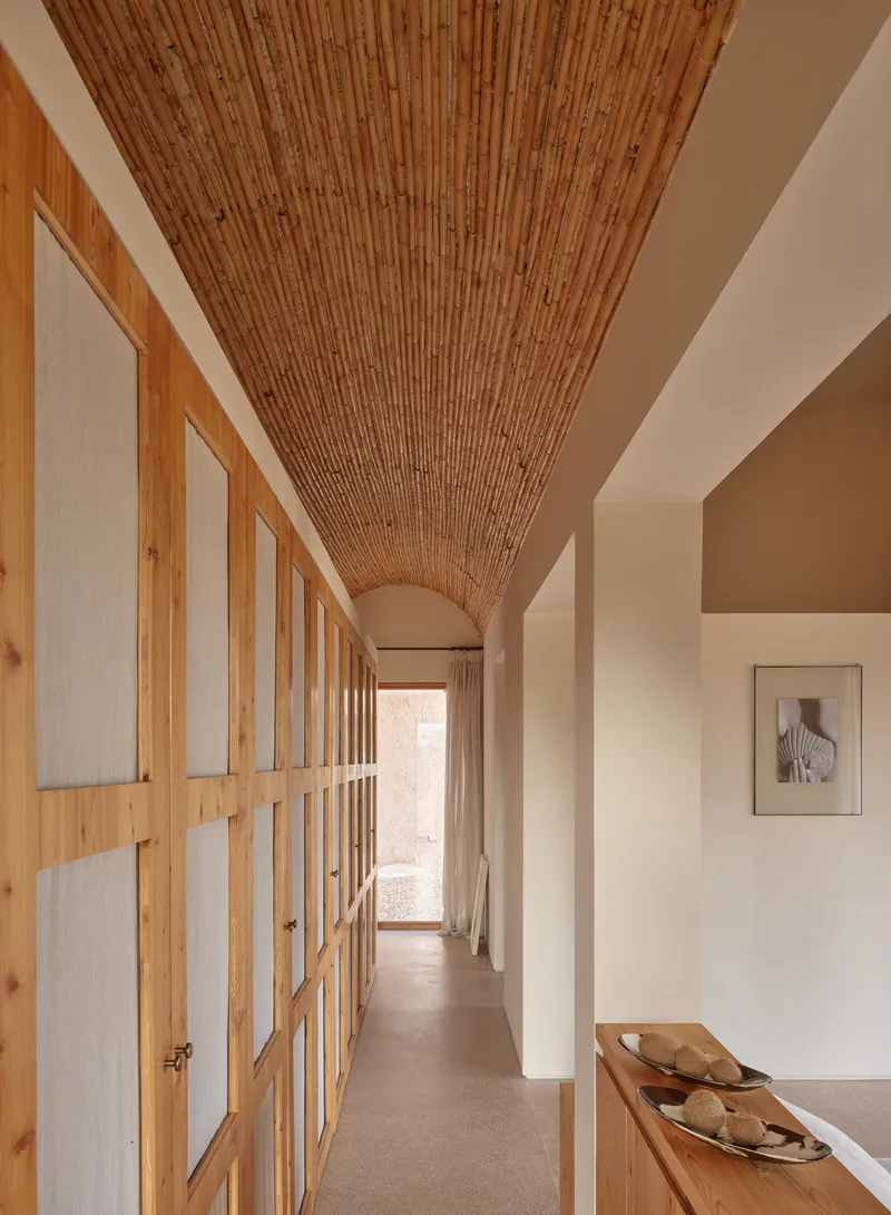 Hallway with continuous bamboo barrel vault ceiling, timber storage doors with frosted panels, and a framed artwork