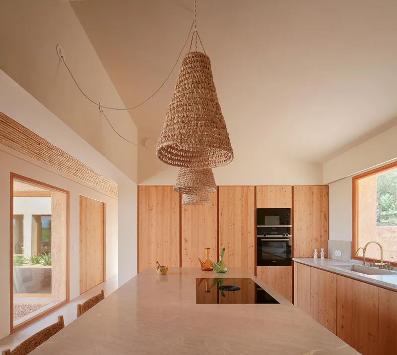 Open kitchen with vaulted ceiling, two-tiered woven pendant fixture, central island, and glazed doors to courtyard