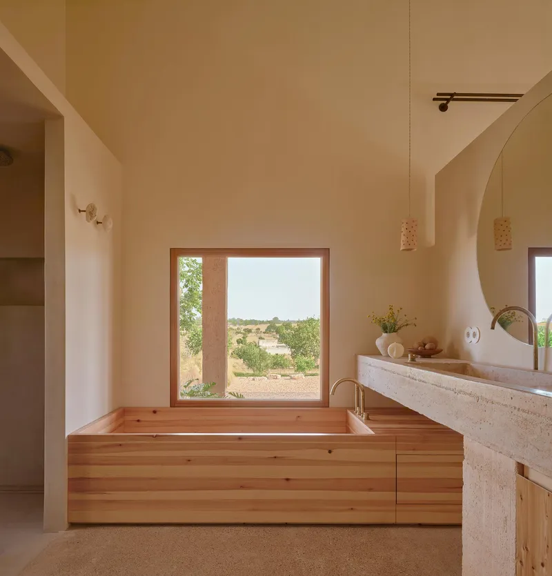 Timber-clad soaking tub positioned beneath a wide window overlooking the arid landscape beyond