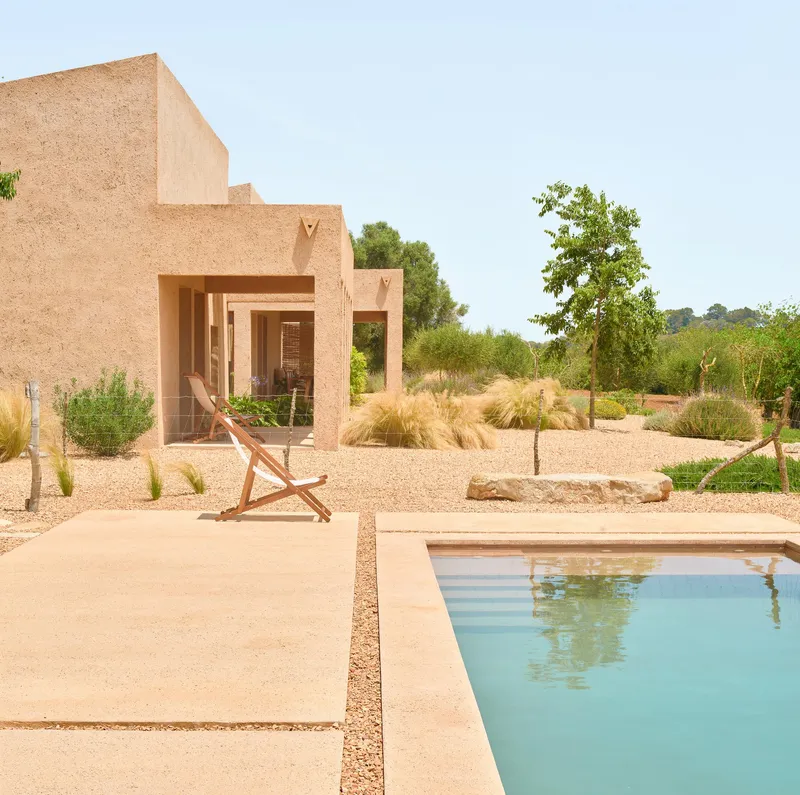 Swimming pool beside terrace with deck chair and straw-textured volumes overlooking gravel garden in daylight