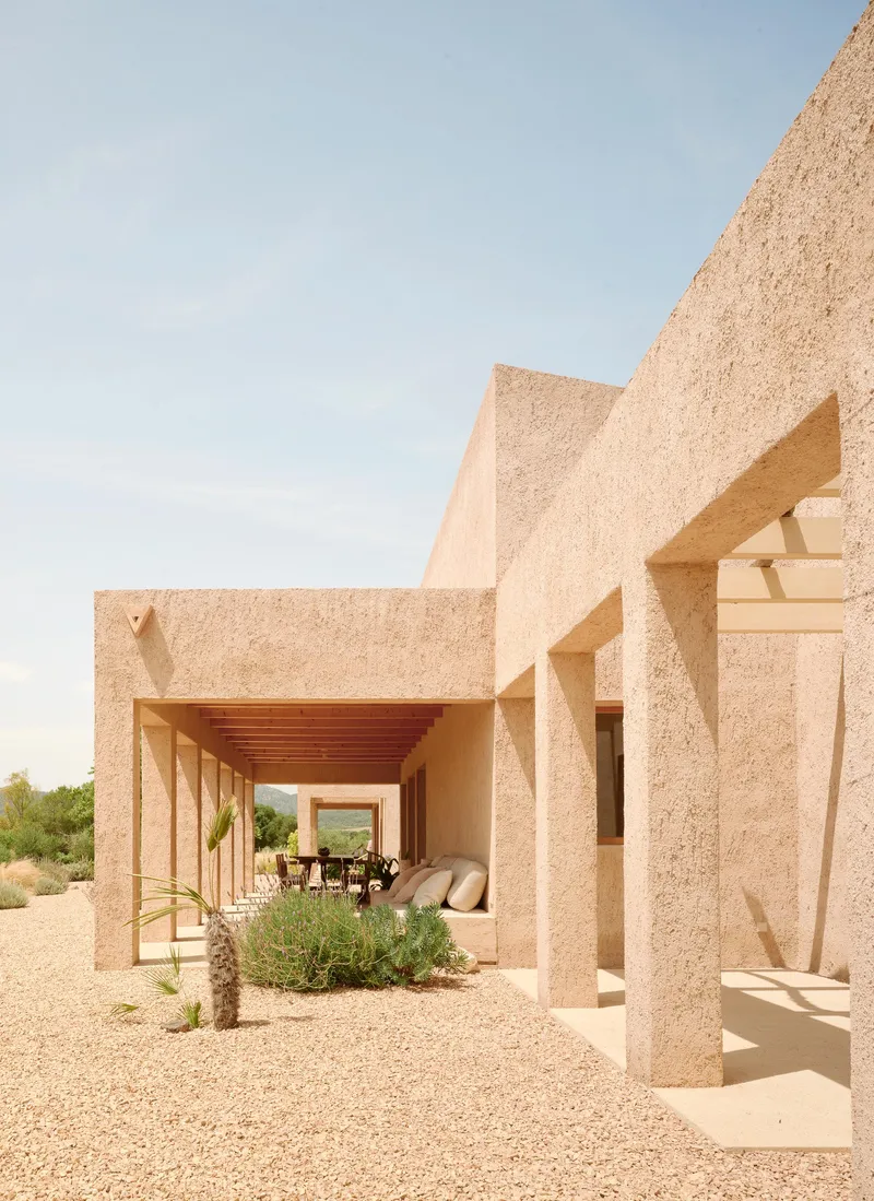 Open timber-beam loggia revealing furnished terrace and distant mountains through aggregate columns