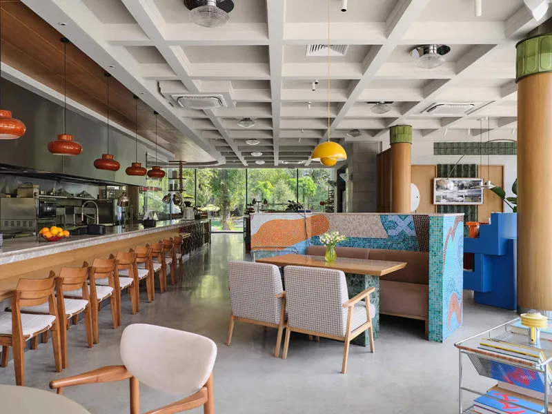 Open dining space with coffered white ceiling, cylindrical timber columns, and floor-to-ceiling glazing overlooking greenery
