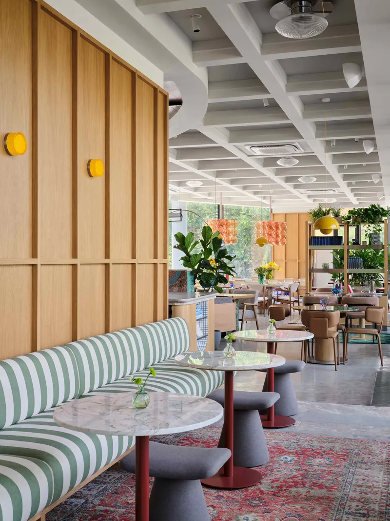 Dining area with coffered ceiling, timber wall panels and green striped banquettes alongside marble-topped tables
