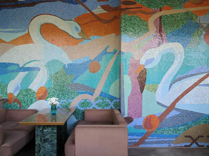 Multicolored mosaic tile mural depicting swans and abstract shapes behind a seating area with taupe armchairs