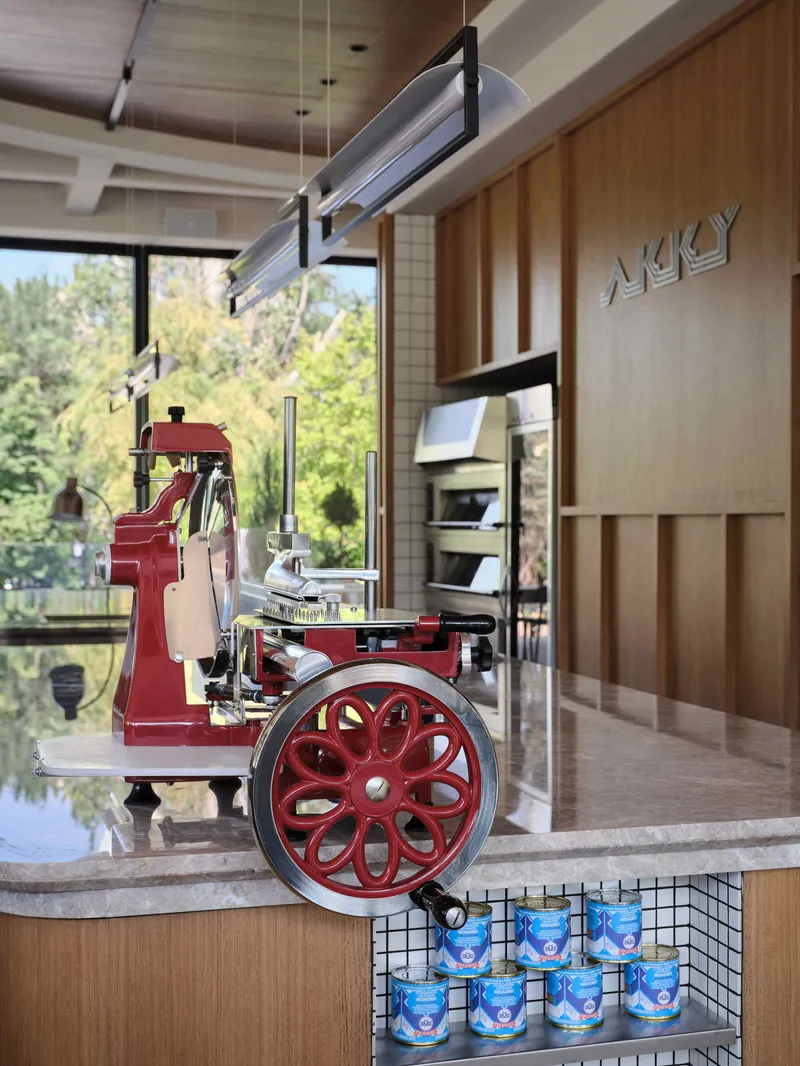 Red vintage espresso machine with spoked wheel on a marble counter near wood paneling and windows