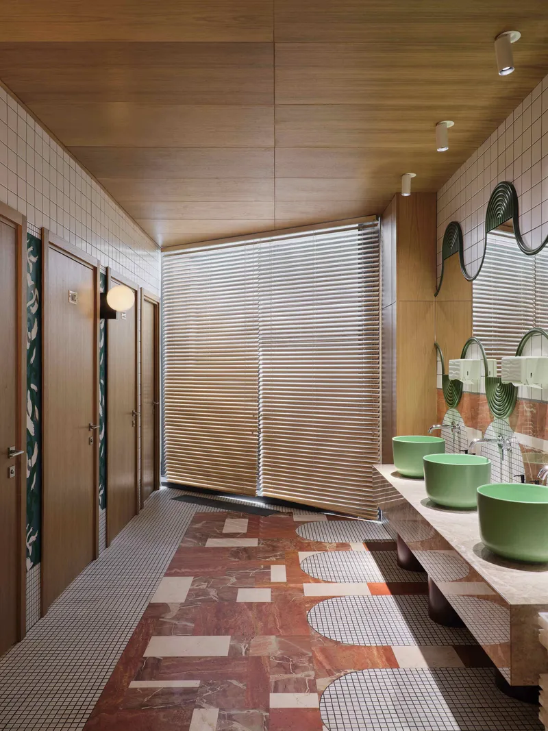 Restroom with green vessel sinks on floating counter and corrugated metal partitions under timber ceiling panels
