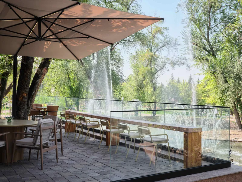 Outdoor terrace with glass balustrade overlooking fountain jets and trees on a summer day